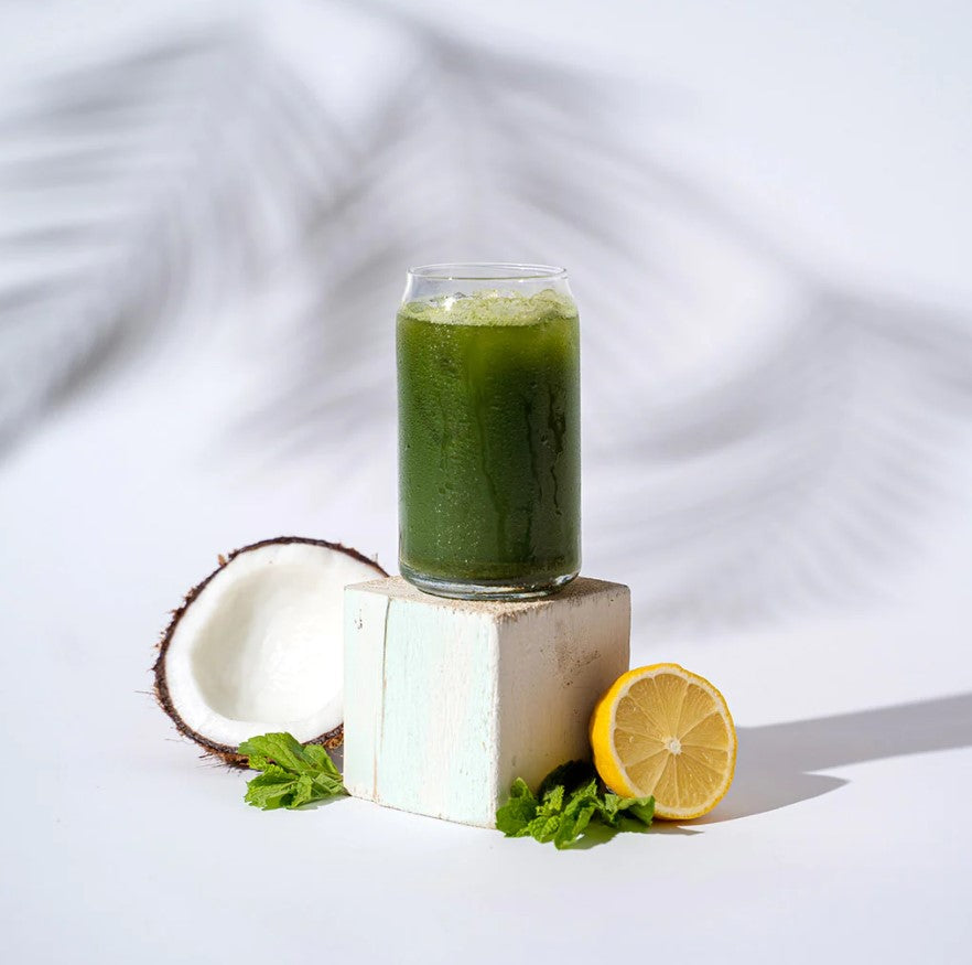 a glass of Organifi Green Juice on a wooden block with a coconut and lemon under it