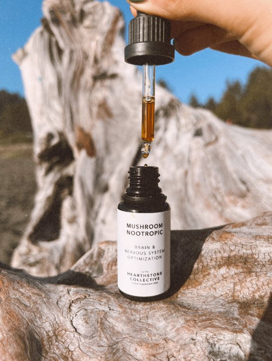 an opened flask of Mushroom Nootropic on a tree stump with someone pouring drops into the flask