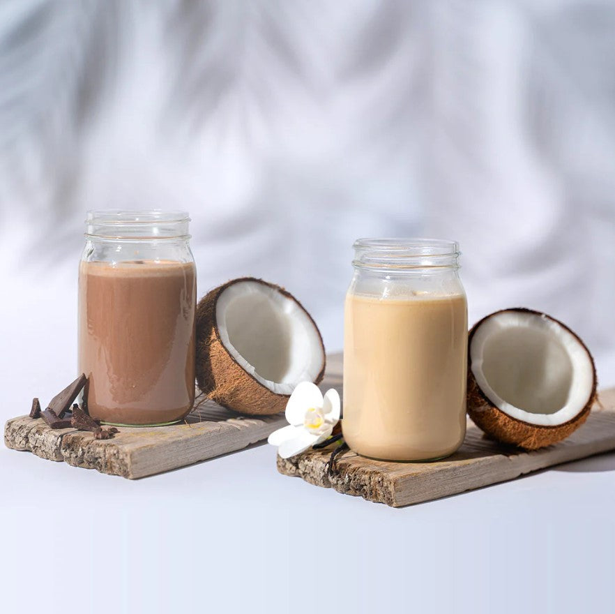 two jars filled with chocolate milk and vanilla milk resting on a piece of wood with coconuts next to the jars