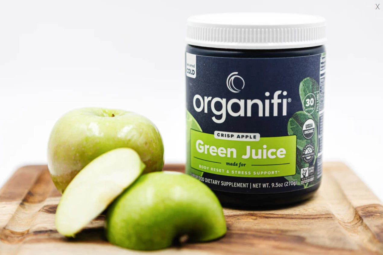 a canister of Organifi Green Juice Crisp Apple on a cutting board with apples next to it